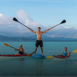A man stands up on a paddle board and 2 women kayaking on Kri Island