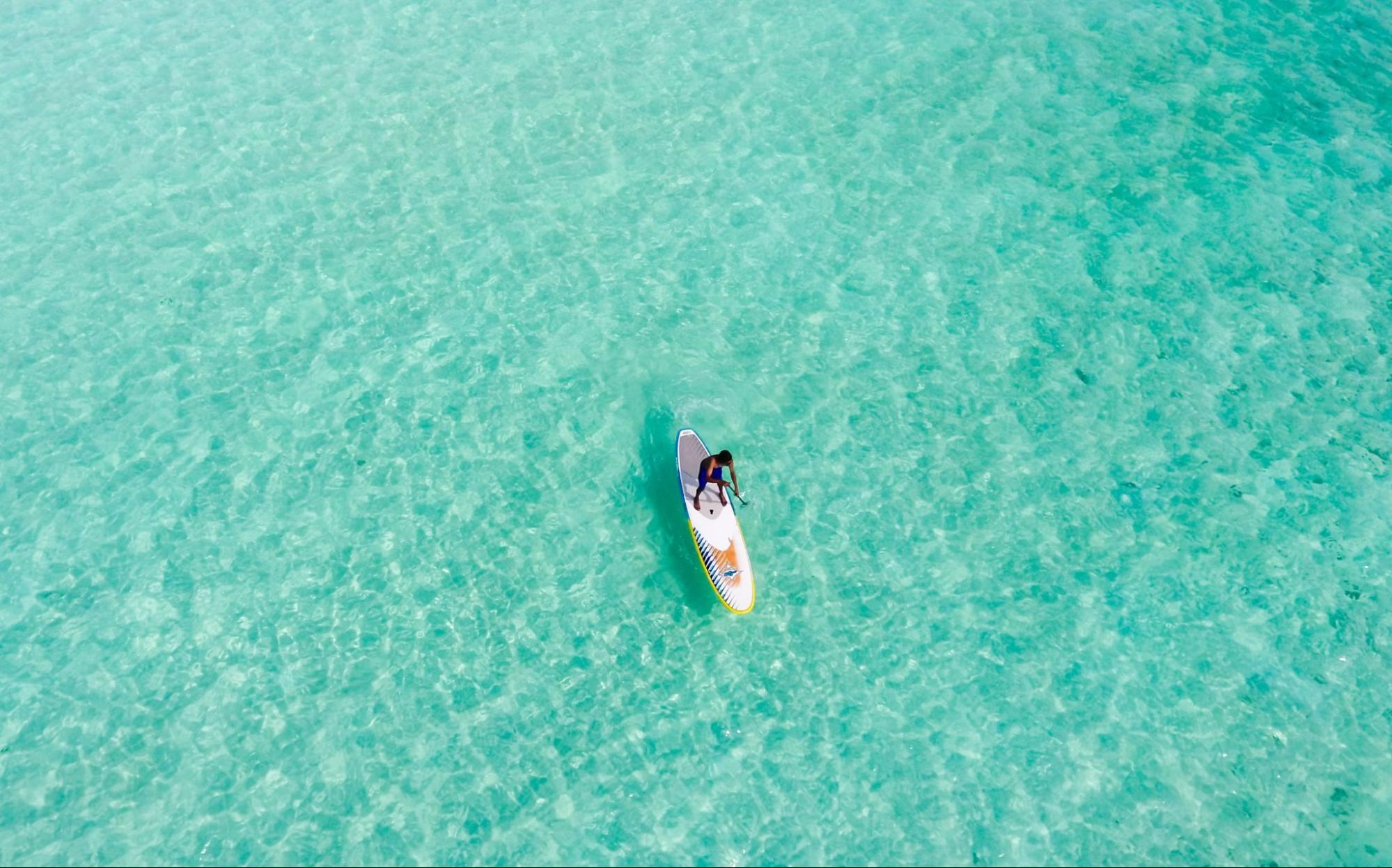 man stand-up paddleboarding at sea with clear blue water